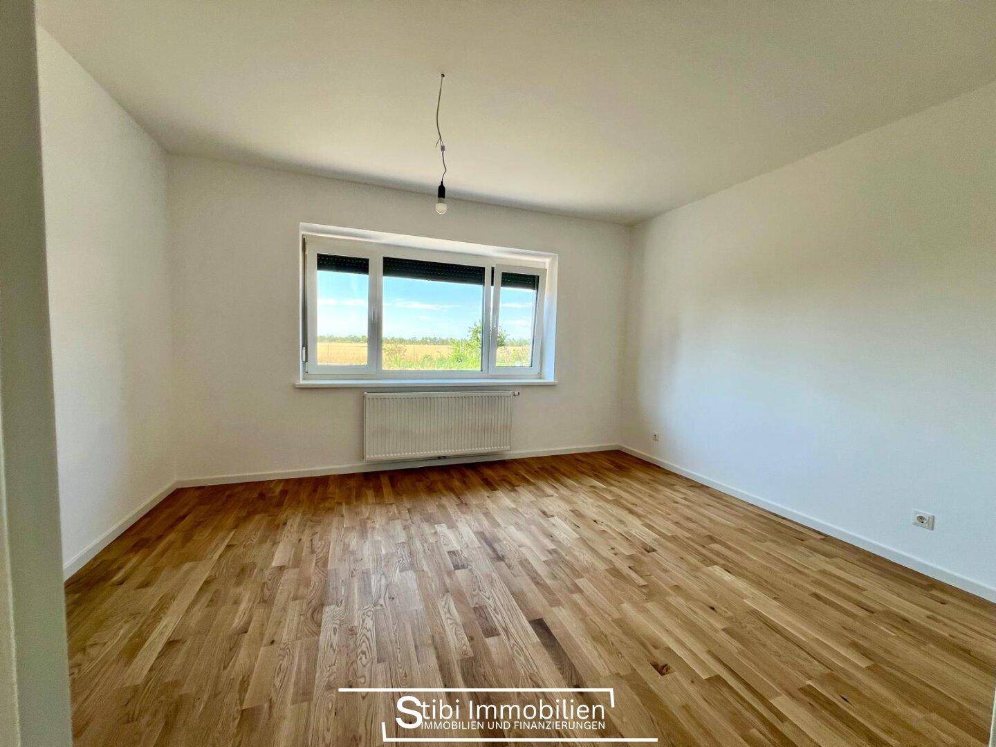 Geräumiges Schlafzimmer mit Holzboden und großem Fenster, das viel Tageslicht hereinlässt.