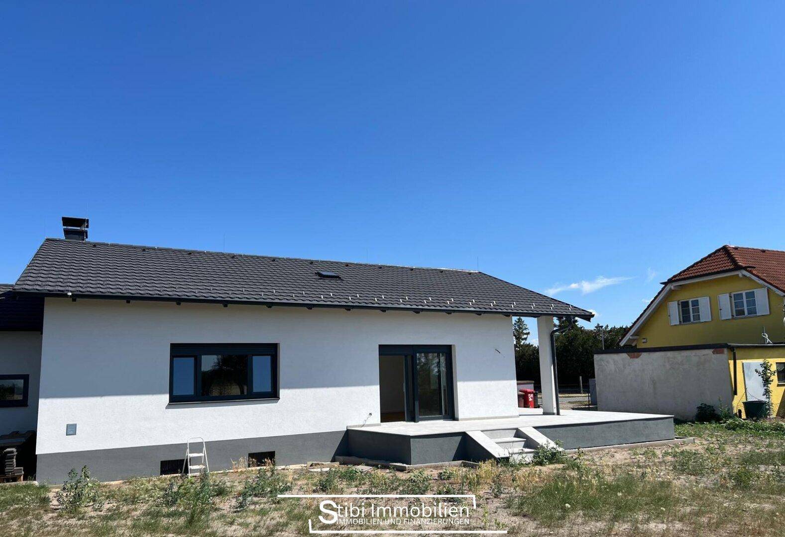 Rückansicht des Hauses mit Terrasse und angrenzendem, noch ungestaltetem Gartenbereich.