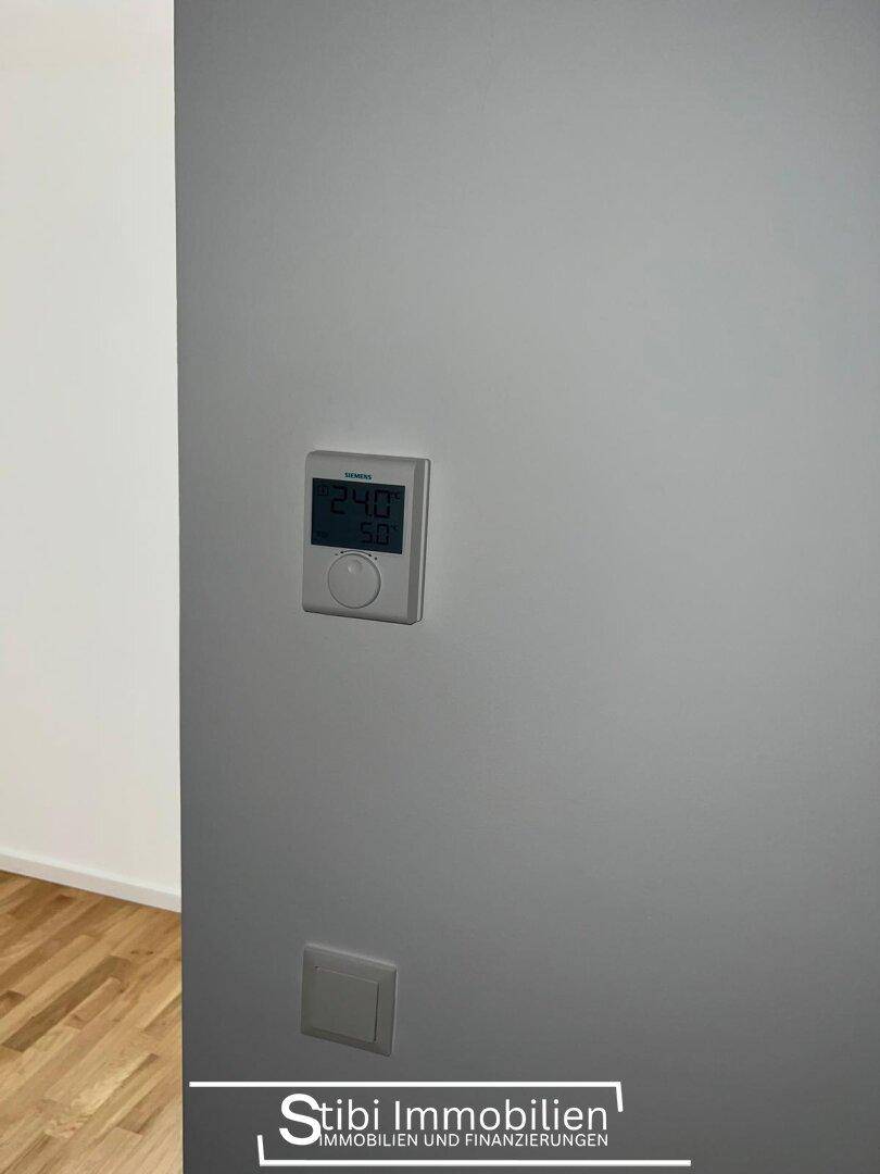 Nahaufnahme eines modernen Thermostats an einer grauen Wand zur Temperaturregelung.