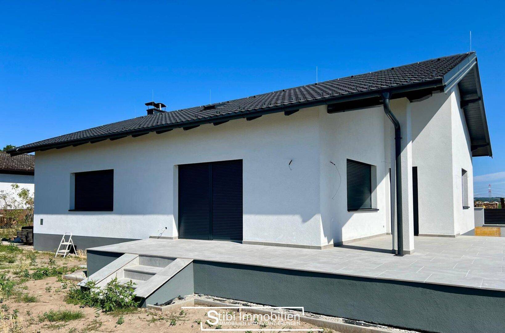 Rückseite des modernen Hauses mit großer gepflasterter Terrasse und Zugang zum Gartenbereich.