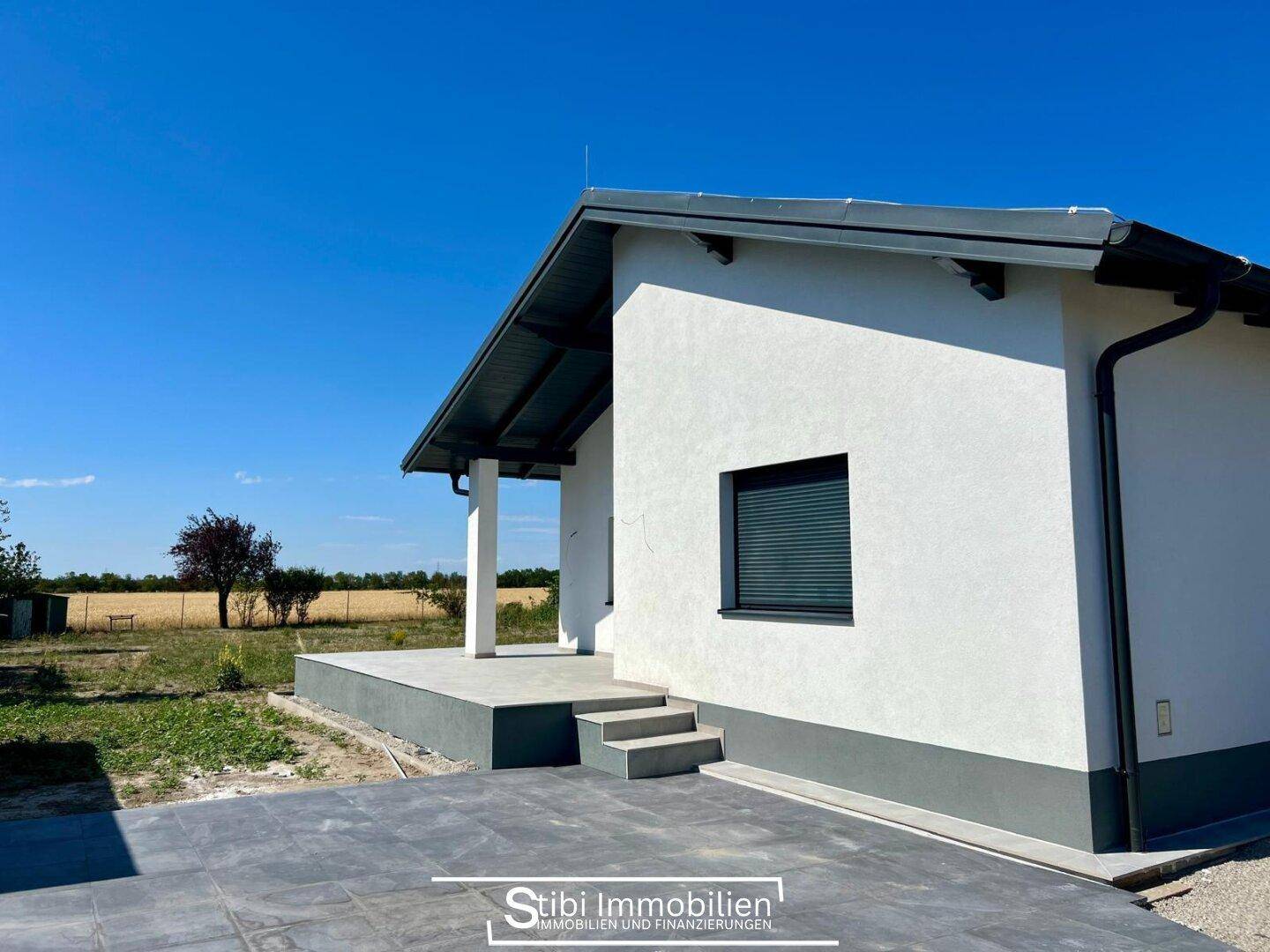 Vorderansicht des modernen Hauses mit überdachtem Eingangsbereich und Blick auf die umliegende Landschaft.