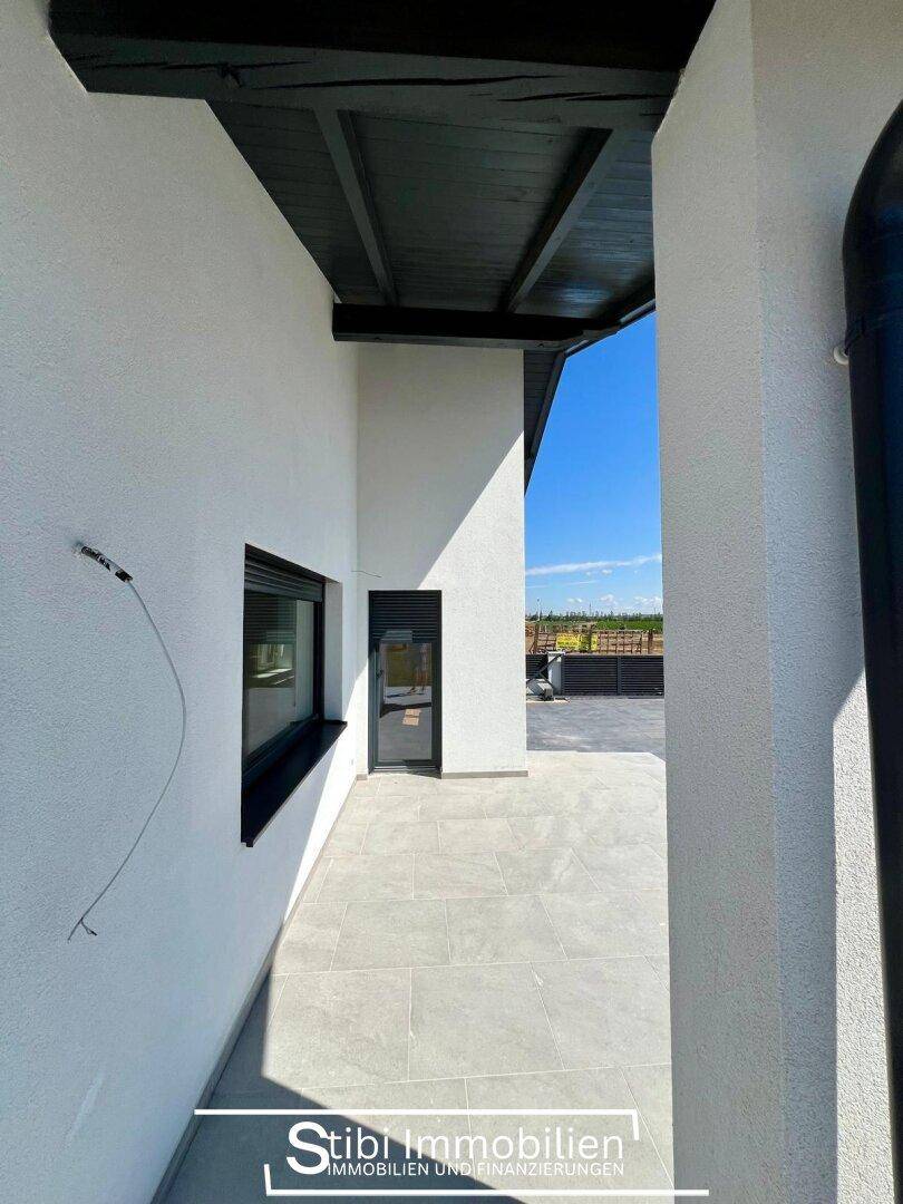 Überdachter Terrassenbereich mit Fliesenboden und Zugang zum Haus, ideal für entspannte Stunden im Freien.