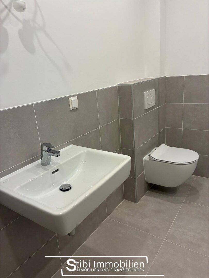 Helles Badezimmer mit modernem Waschbecken und wandhängendem WC, ausgestattet mit grauen Fliesen.
