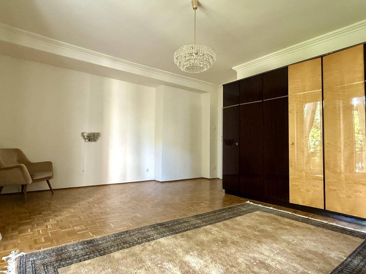 Geräumiges Zimmer mit Parkettboden, großem Kleiderschrank und Kronleuchter.
