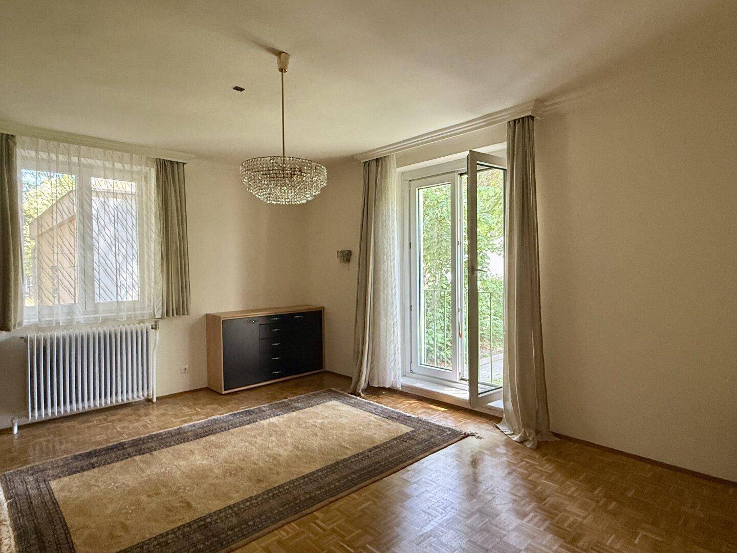 Helles Wohnzimmer mit Parkettboden, Kronleuchter und Zugang zu einem Balkon oder einer Terrasse.