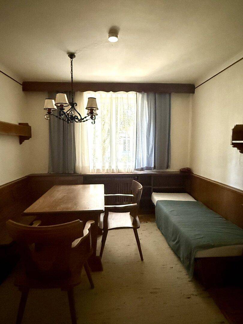 Kleines Zimmer mit Einzelbett, Holztisch und Fenster, ideal als Gäste- oder Kinderzimmer.