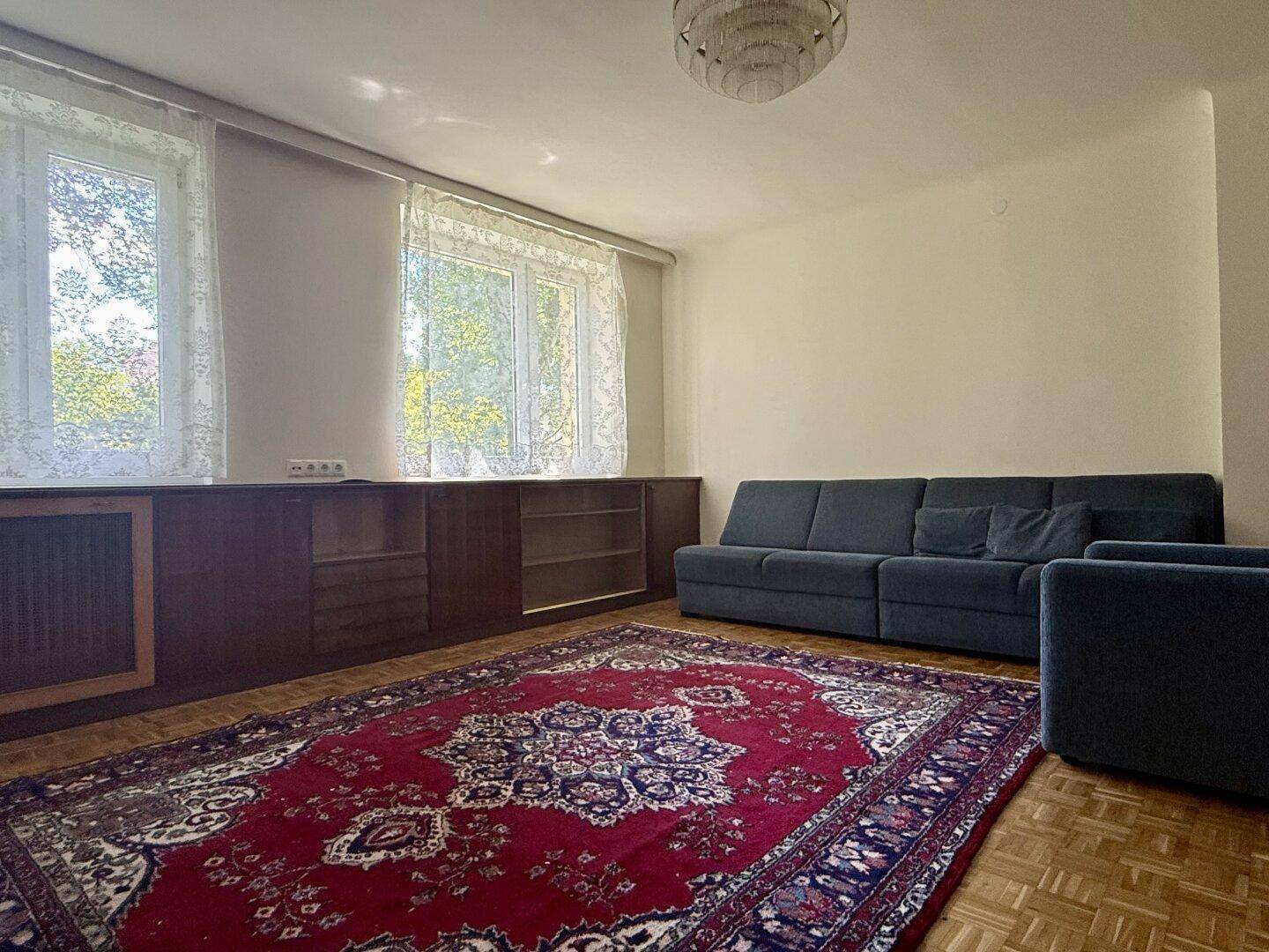 Gemütliches Wohnzimmer mit Sofa, Teppich und großen Fenstern für viel Tageslicht.