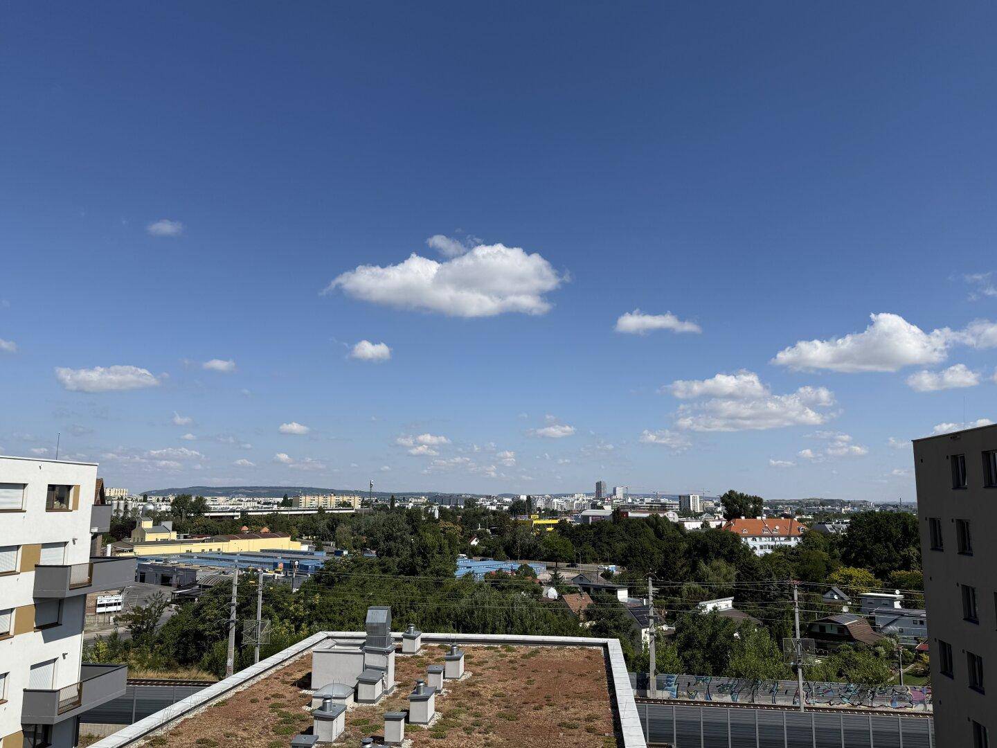 Weitläufiger Blick über die Stadt und umliegende Gebäude unter blauem Himmel.
