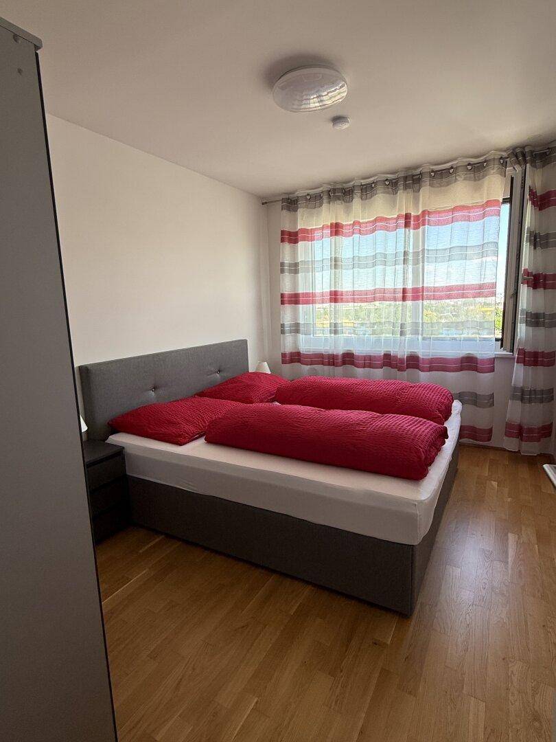 Schlafzimmer mit Doppelbett, roten Bettdecken und Holzparkettboden.