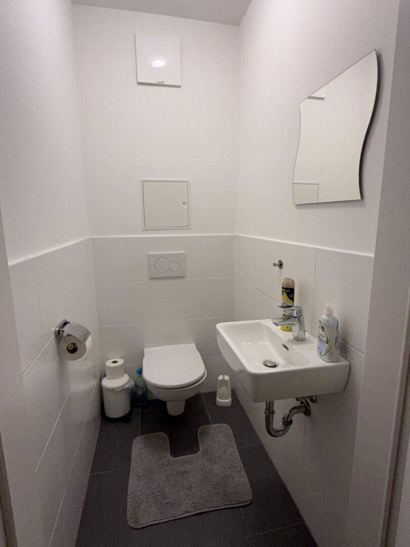 Modernes Gäste-WC mit Wand-WC, kleinem Waschbecken und Spiegel.