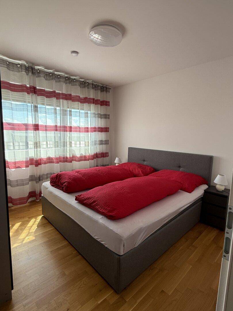 Helles Schlafzimmer mit Doppelbett, roten Bettdecken und Parkettboden.