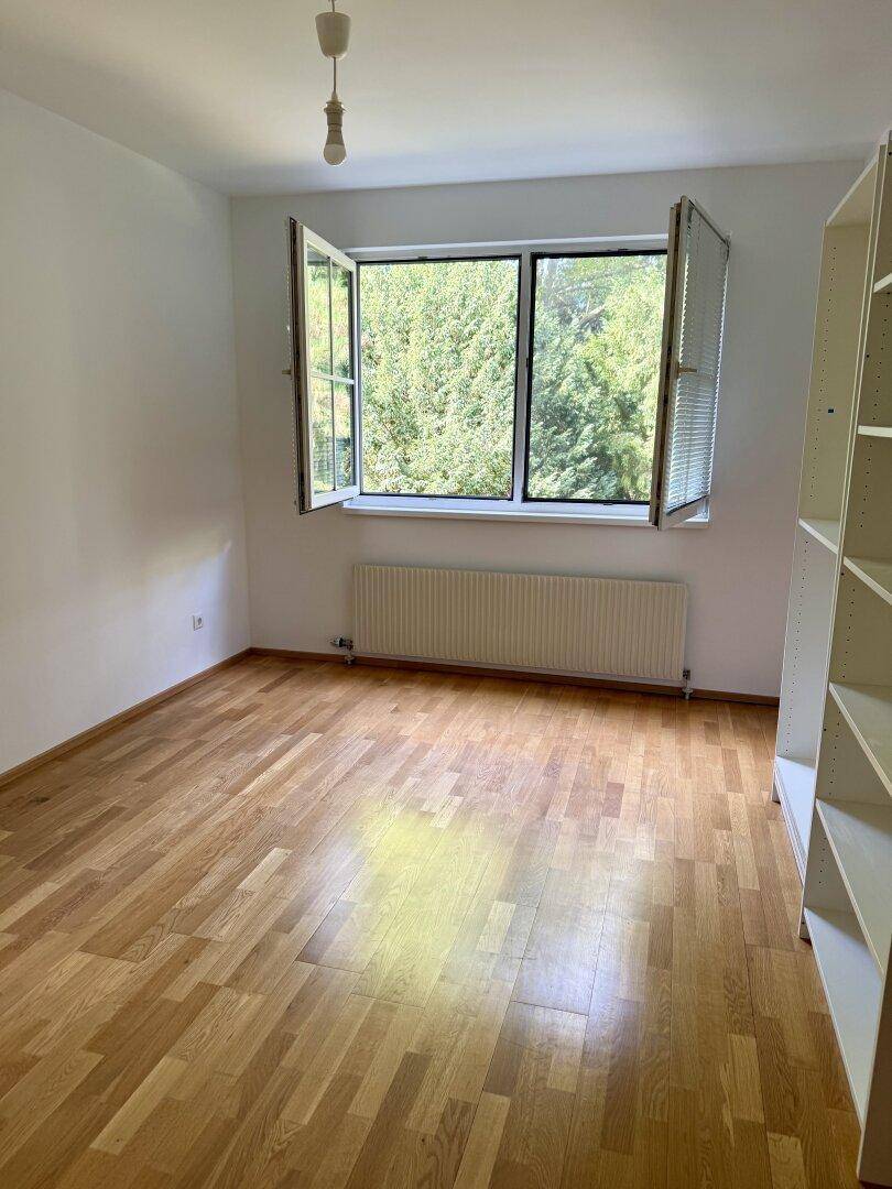 Helles Zimmer mit Parkettboden, großem Fenster und Blick ins Grüne, ideal als Schlaf- oder Arbeitszimmer.