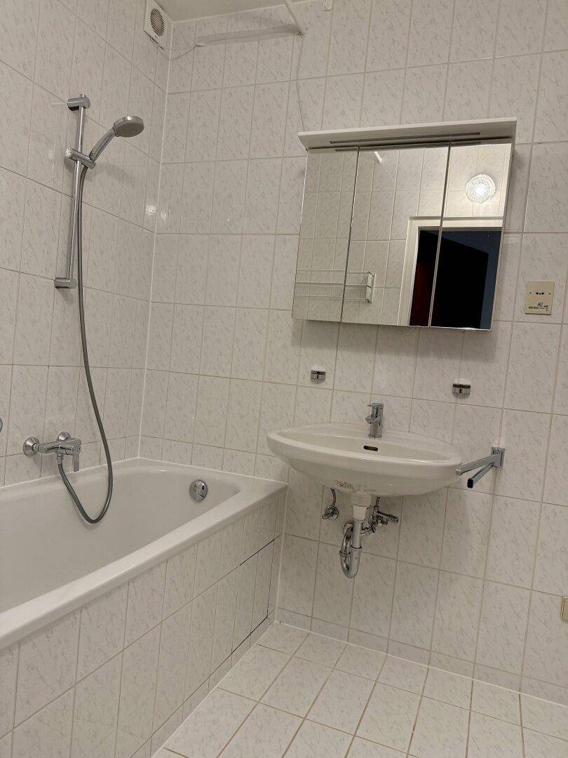 Gefliestes Badezimmer mit Badewanne, Duschfunktion, Waschbecken und Spiegelschrank.