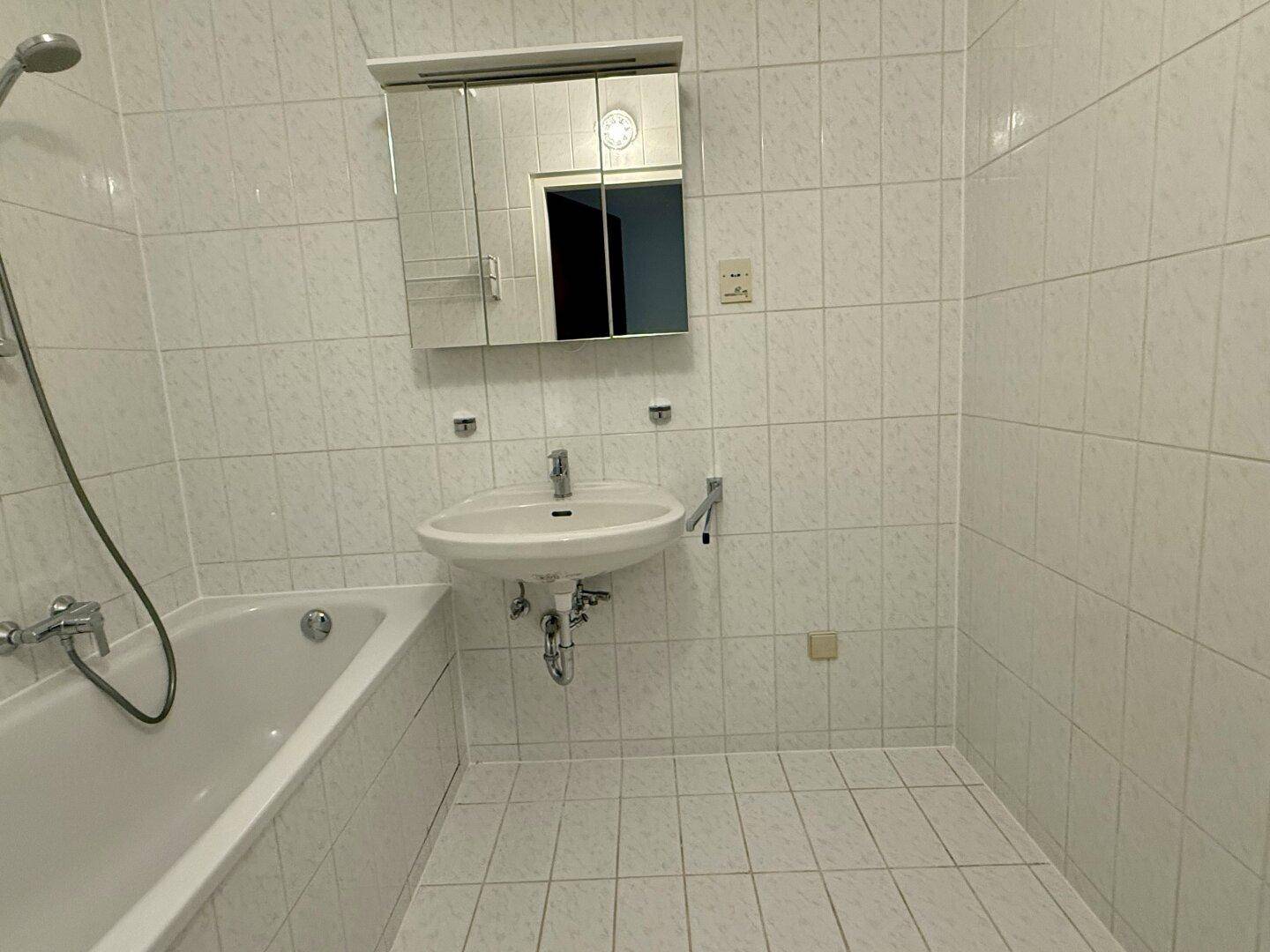 Helles Badezimmer mit weißen Fliesen, Badewanne mit Duscharmatur und praktischem Spiegelschrank.