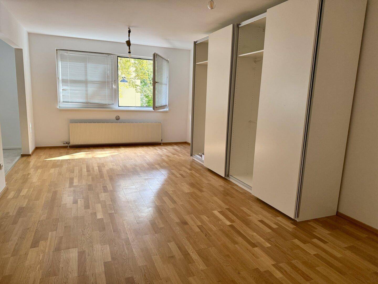 Geräumiges Schlafzimmer mit hellem Parkettboden, großen Fenstern und praktischen Einbauschränken.