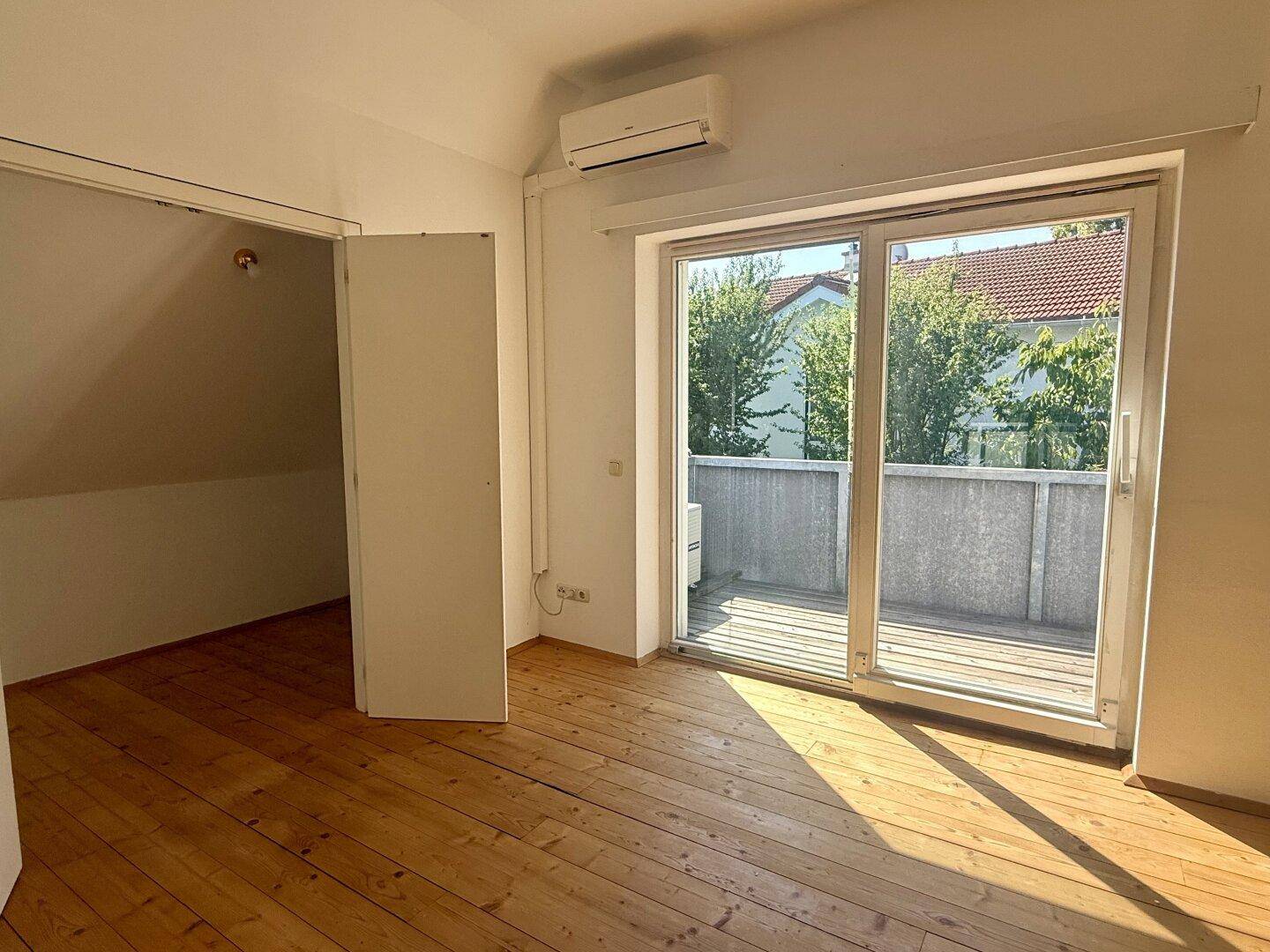 Helles Schlafzimmer mit Holzdielenboden, Klimaanlage und Zugang zur Terrasse.