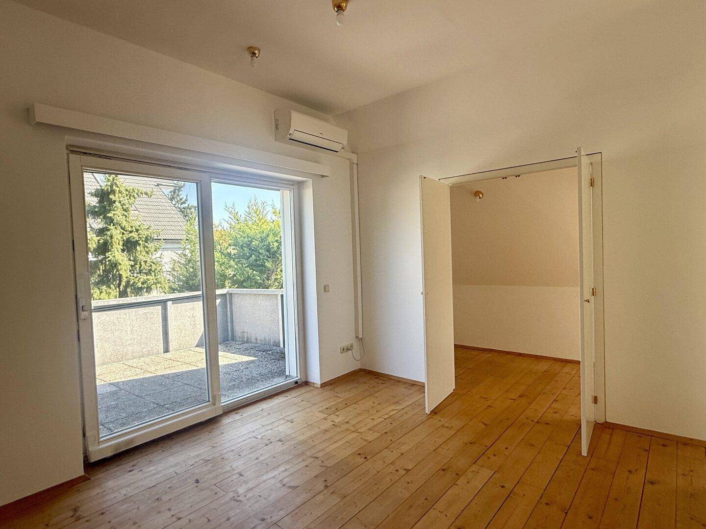 Geräumiges Schlafzimmer mit Holzdielenboden, Klimaanlage und großem Terrassenzugang.
