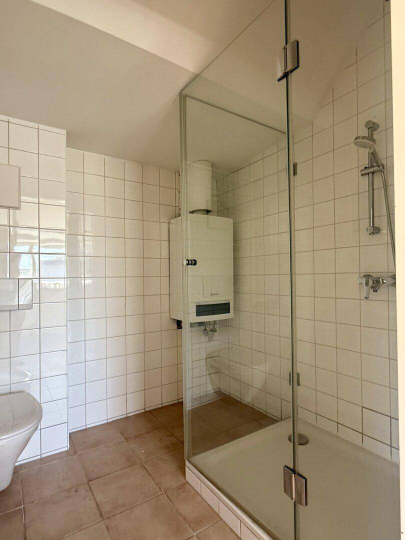 Badezimmer mit Duschkabine, WC und weiß gefliesten Wänden.