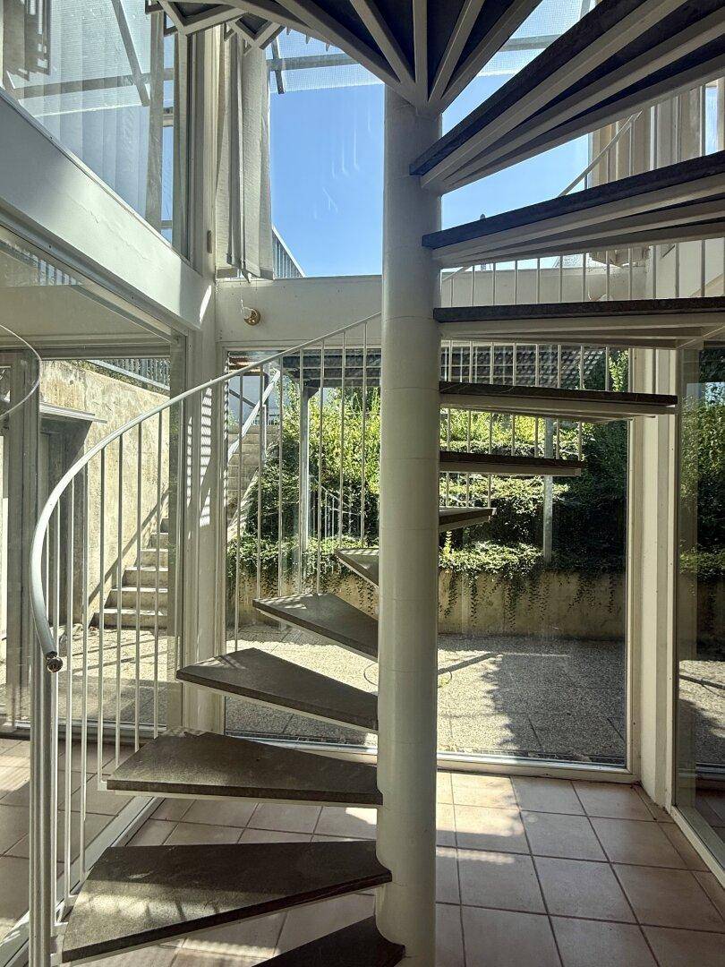 Moderne Wendeltreppe in einem lichtdurchfluteten Bereich mit großen Glasflächen.