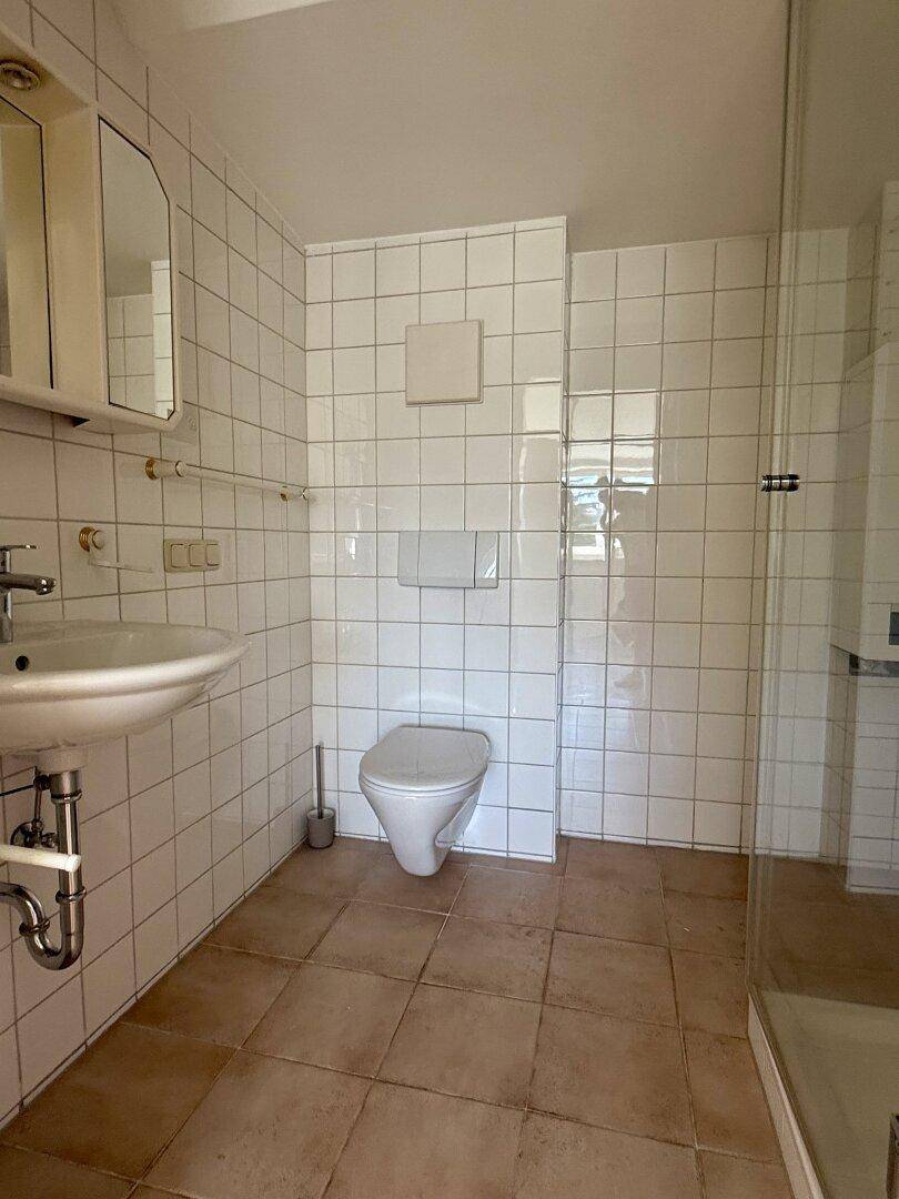Helles Badezimmer mit Waschbecken, WC, Spiegelschrank und weißem Fliesenspiegel.