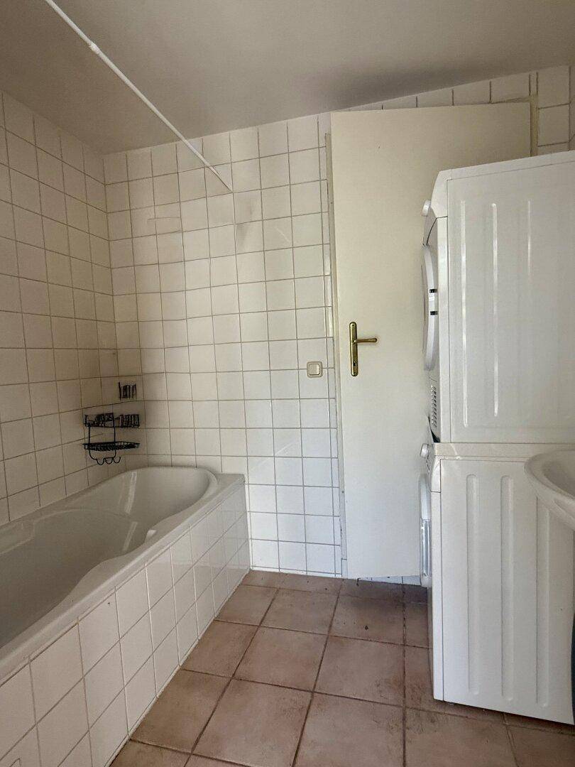 Badezimmer mit Badewanne, Waschmaschine und Trockner, weiß gefliest.