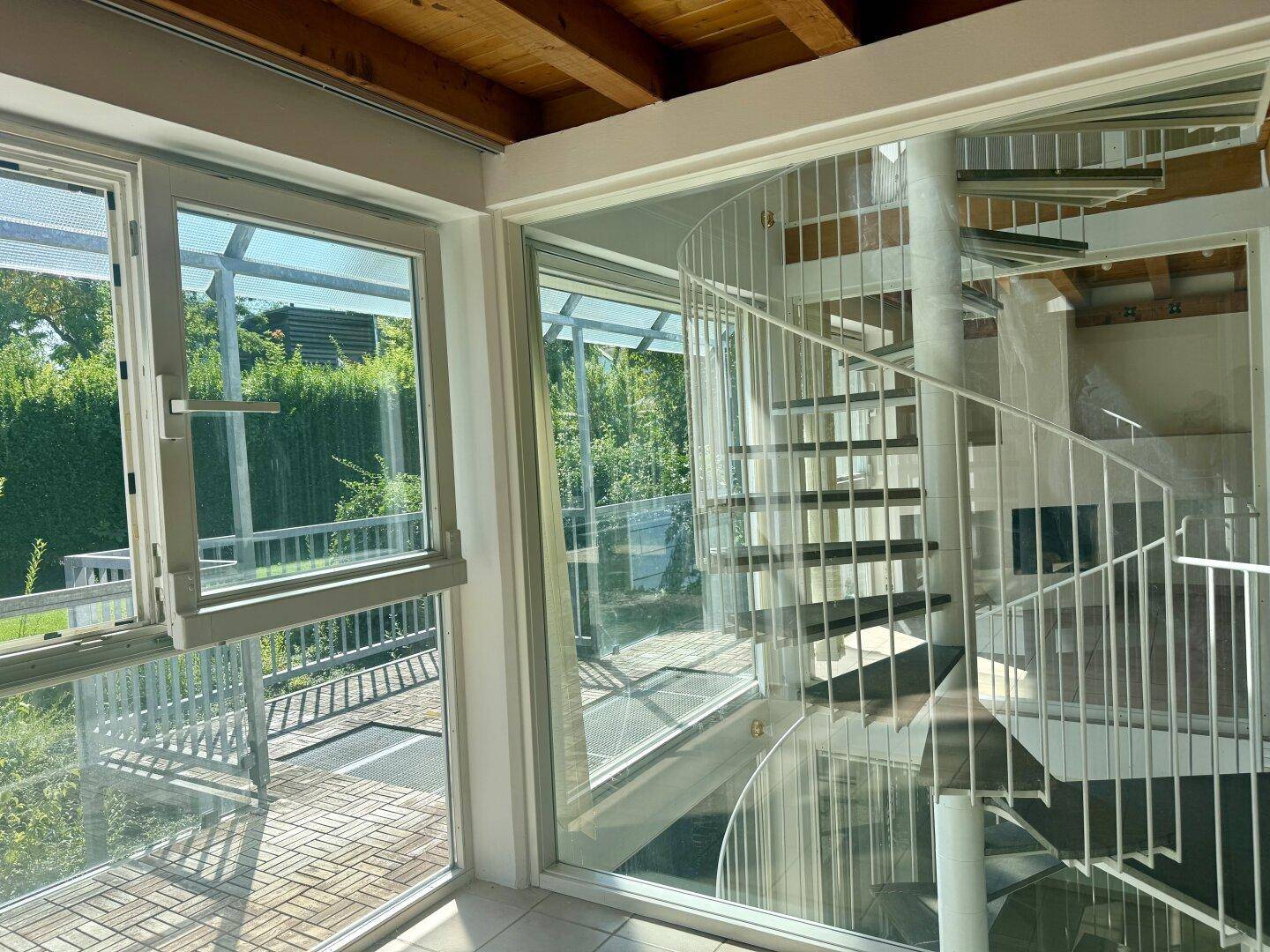 Lichtdurchfluteter Treppenbereich mit Wendeltreppe und großen Glasfronten.