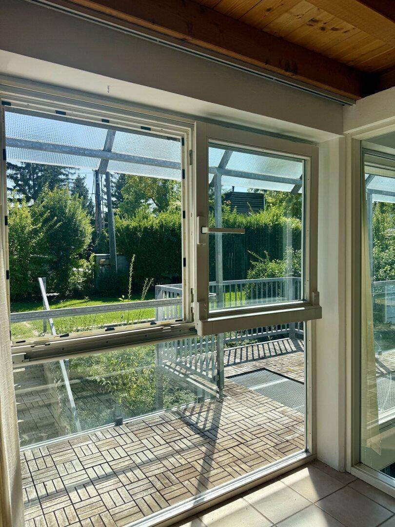 Überdachter Balkon mit Holzboden und Blick in den grünen Gartenbereich.