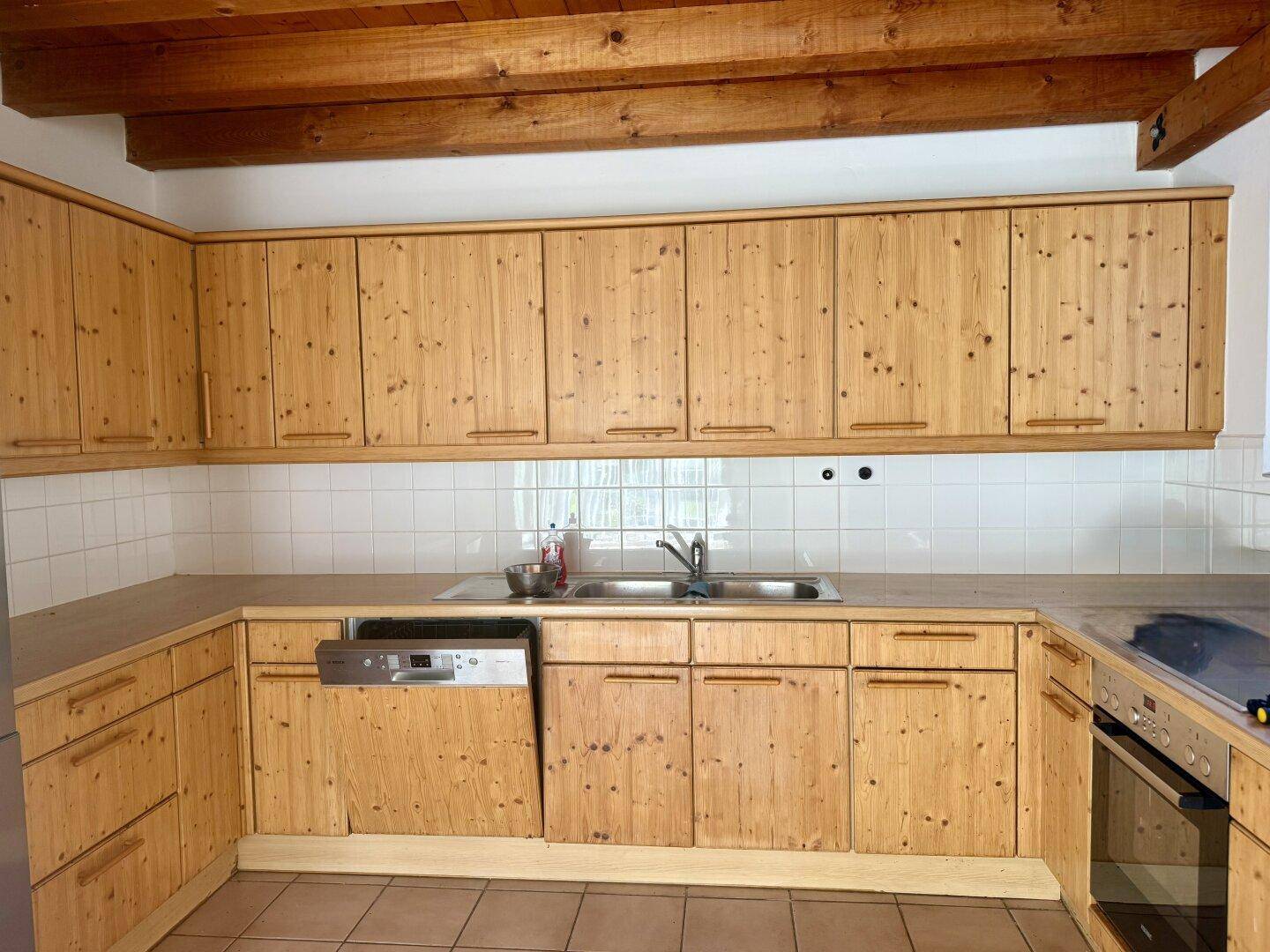 Traditionelle Holzküche mit Einbaugeräten, Spülmaschine und weißem Fliesenspiegel.
