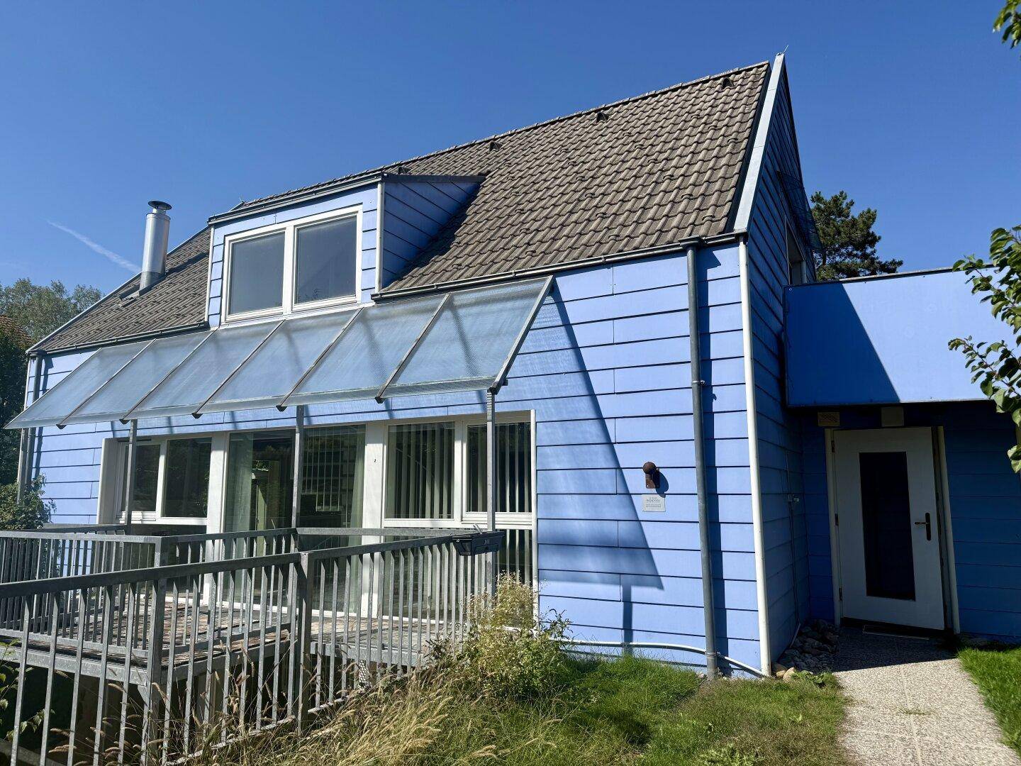 Blau verkleidetes Haus mit Satteldach, Balkon und großen Fenstern.