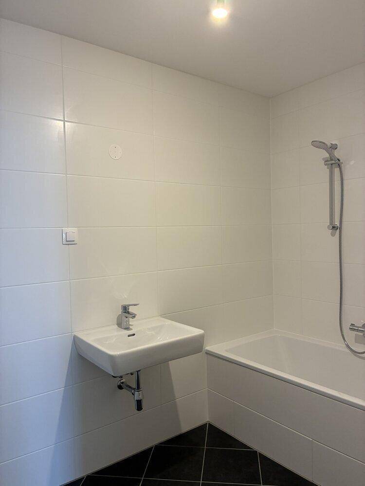Modernes Badezimmer mit weißen Fliesen, schwarzem Boden, Badewanne mit Dusche und Waschbecken.