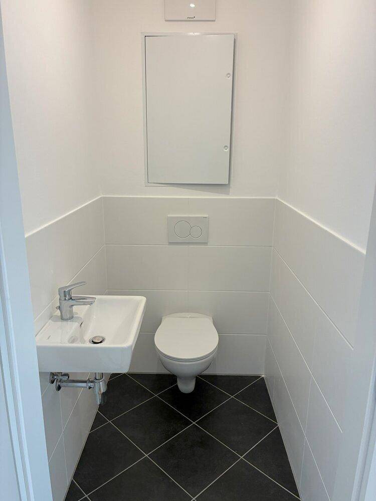 Separates Gäste-WC mit Wand-WC, kleinem Waschbecken und dunklen Bodenfliesen in modernem Design.