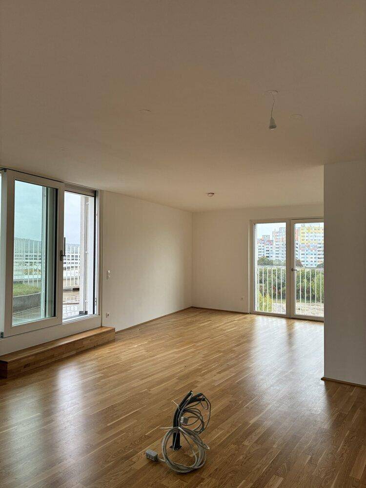 Geräumiges Wohnzimmer mit Parkettboden, weißen Wänden und großen Fenstern zu den Außenbereichen.