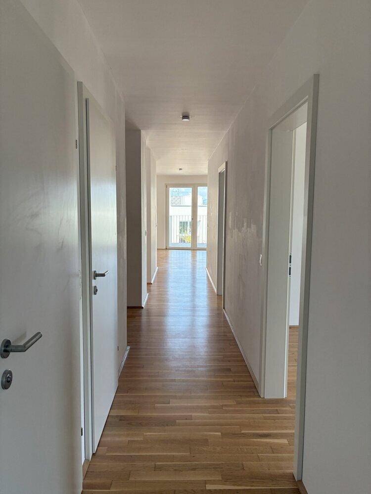 Langer, heller Flur mit Holzboden, der zu weiteren Zimmern und einem Balkon führt.