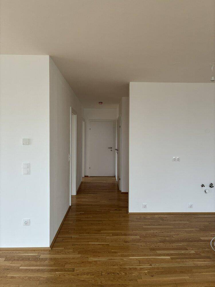 Heller Flur mit Parkettboden und weißen Wänden, der zu den verschiedenen Zimmern der Wohnung führt.