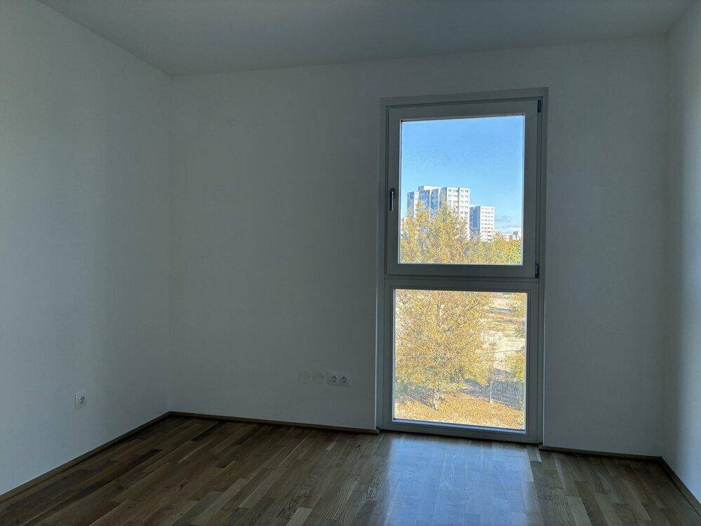 Schlafzimmer mit Holzboden und großem Fenster, das einen Blick auf die Umgebung bietet.