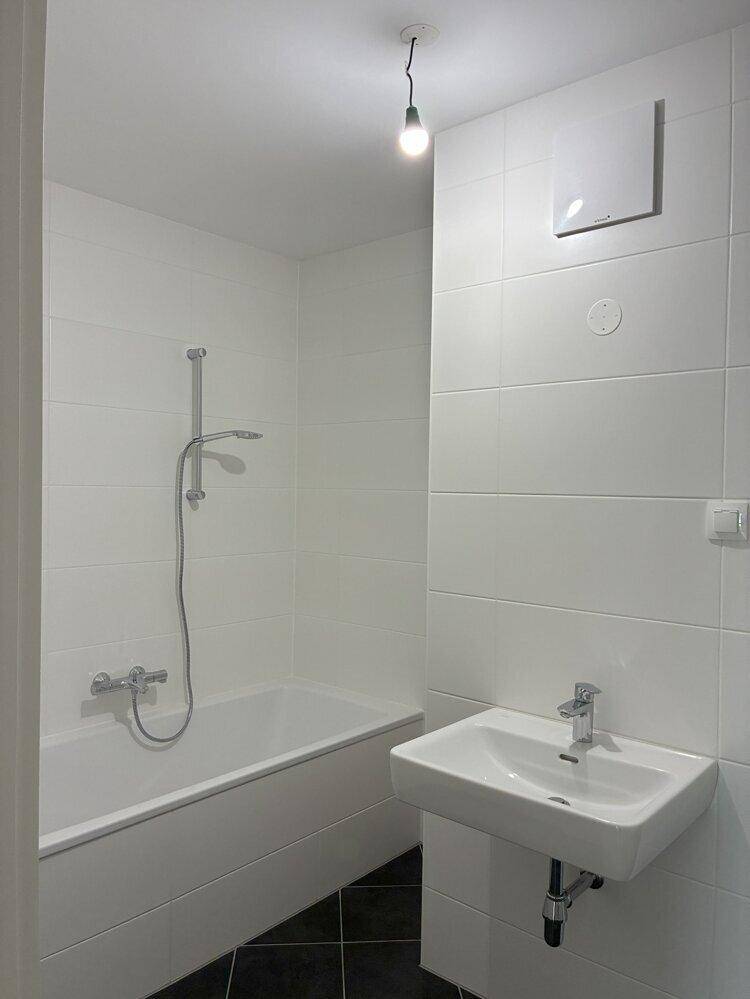 Helles Badezimmer mit Badewanne, Waschbecken und weißen Fliesen, kombiniert mit dunklem Boden.