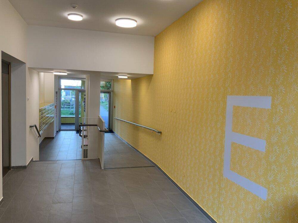 Heller Eingangsbereich eines Mehrfamilienhauses mit gelber Wandgestaltung und barrierefreier Rampe.