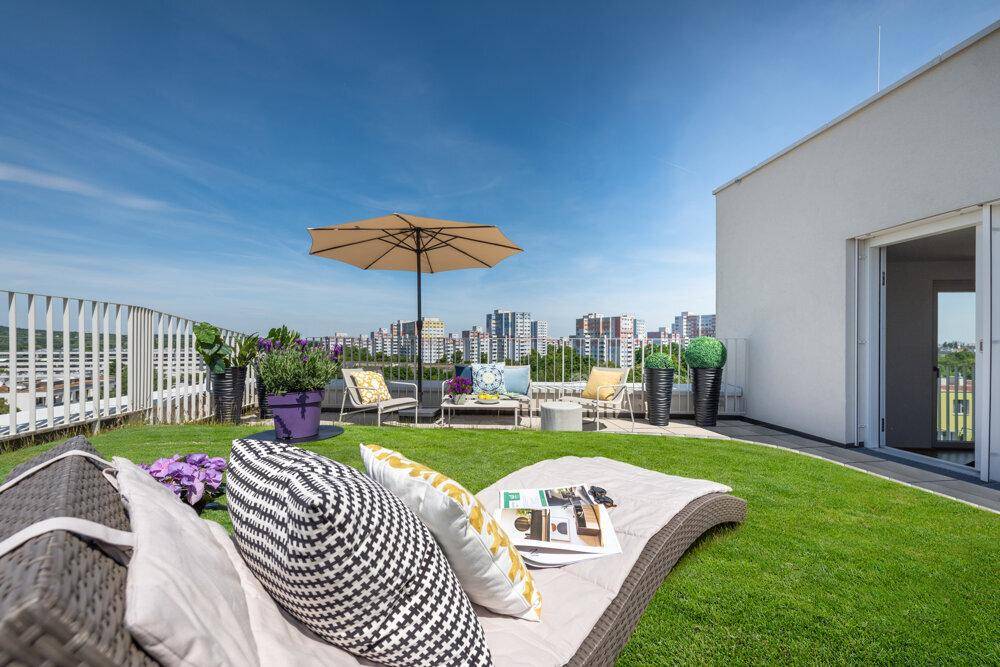 Sonniger Dachgarten mit bequemen Lounge-Möbeln, Sonnenschirm und weitem Blick über die Stadt.