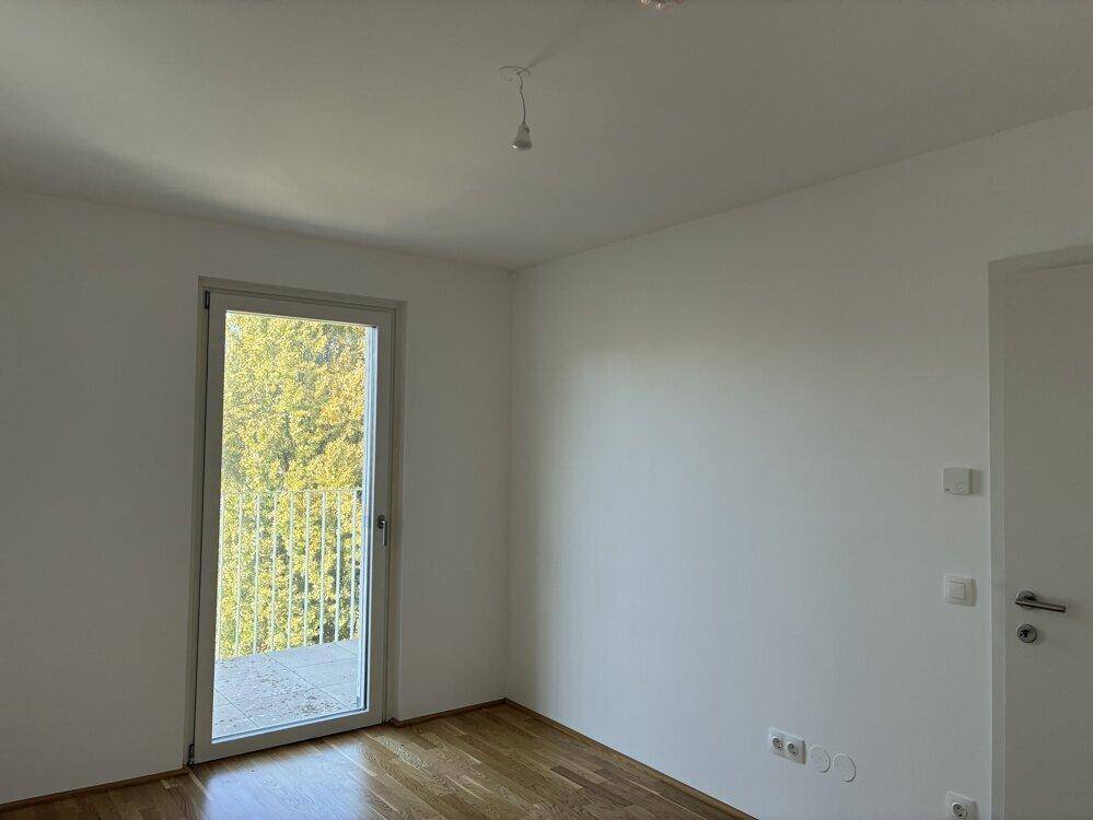 Helles Zimmer mit Parkettboden und Zugang zu einem französischen Balkon mit Blick ins Grüne.
