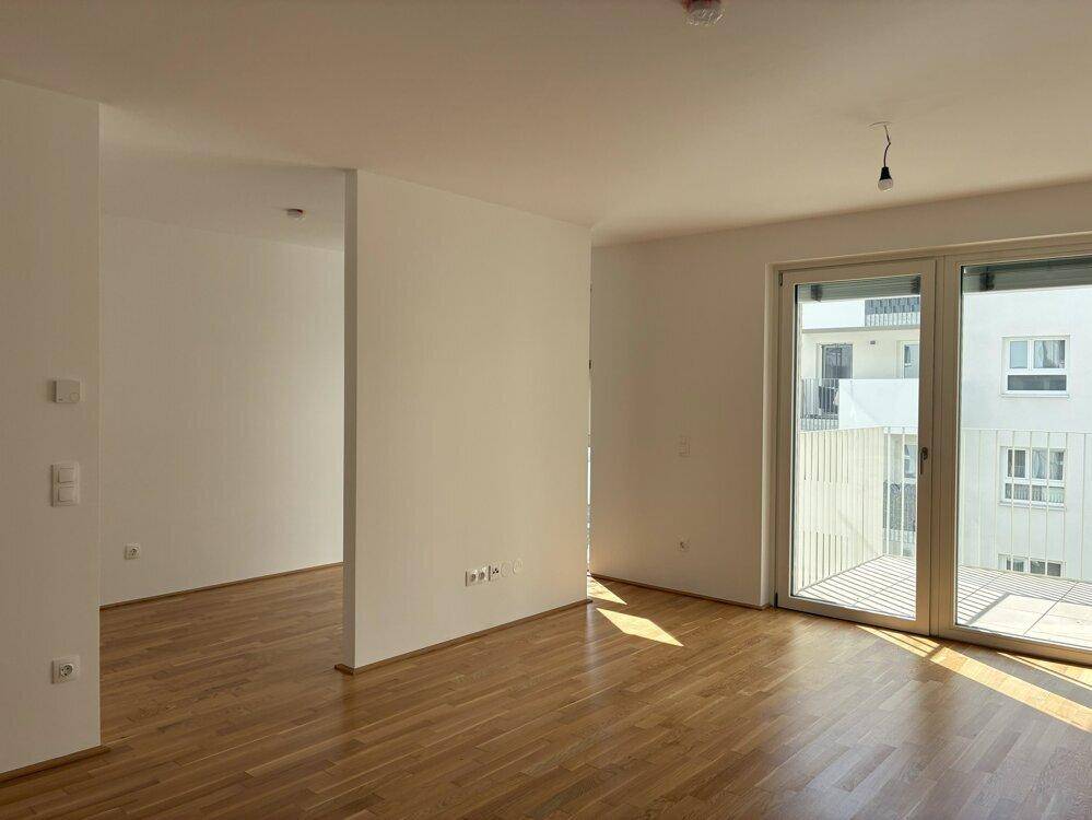 Heller, leerer Raum mit Holzboden und Zugang zu einem Balkon, ideal für ein Wohnzimmer.
