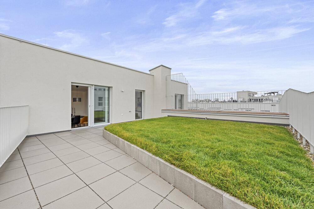 Großzügige Dachterrasse mit Fliesenboden, Rasenfläche und Blick auf die umliegende Stadtlandschaft.