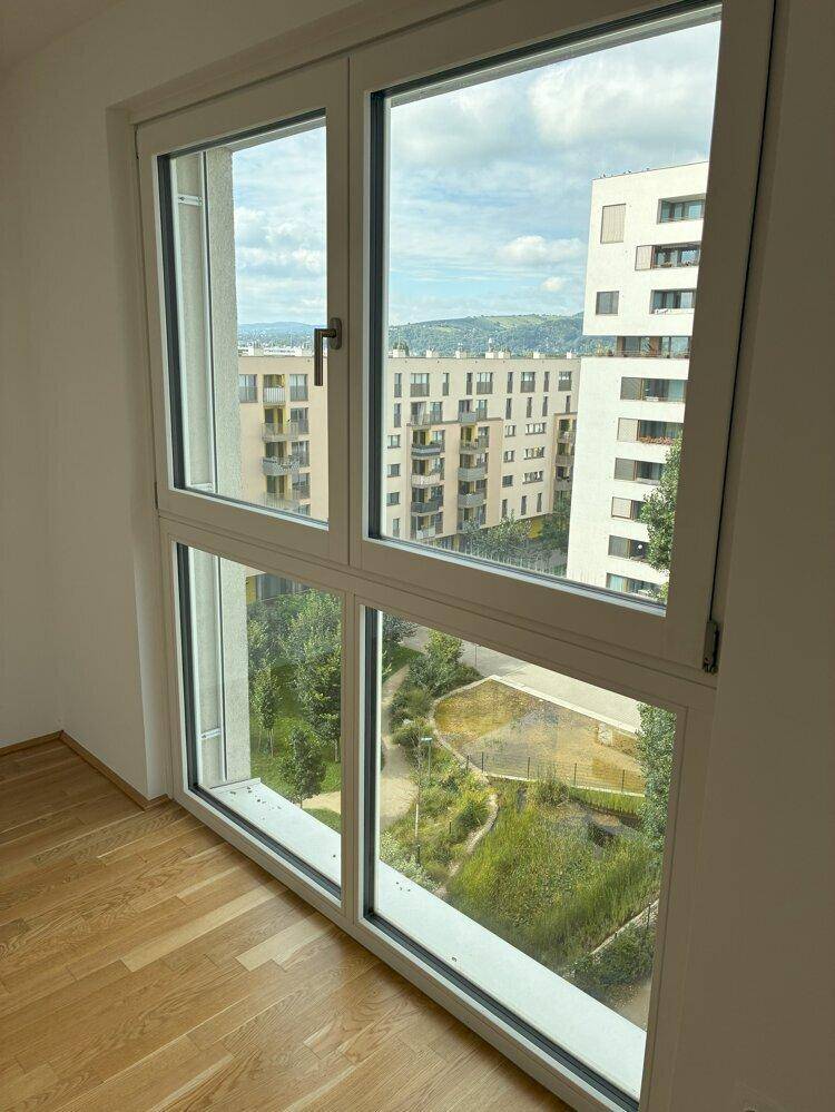 Großes Fenster in einem hellen Raum mit Blick auf moderne Gebäude und einen begrünten Innenhof.