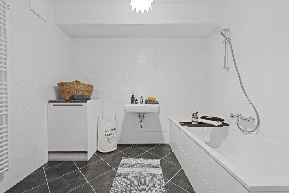 Modernes Badezimmer mit weißen Wandfliesen, dunklem Boden, Badewanne und Waschbecken.