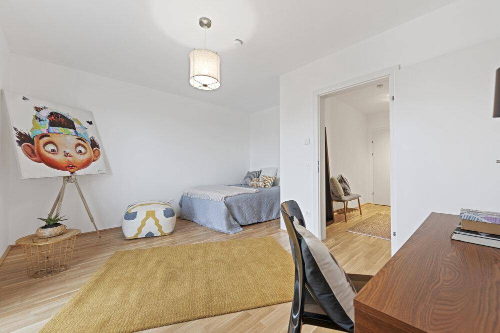 Freundliches Schlafzimmer mit Holzboden und Schreibtisch, das einen offenen Zugang zu einem weiteren Raum bietet.