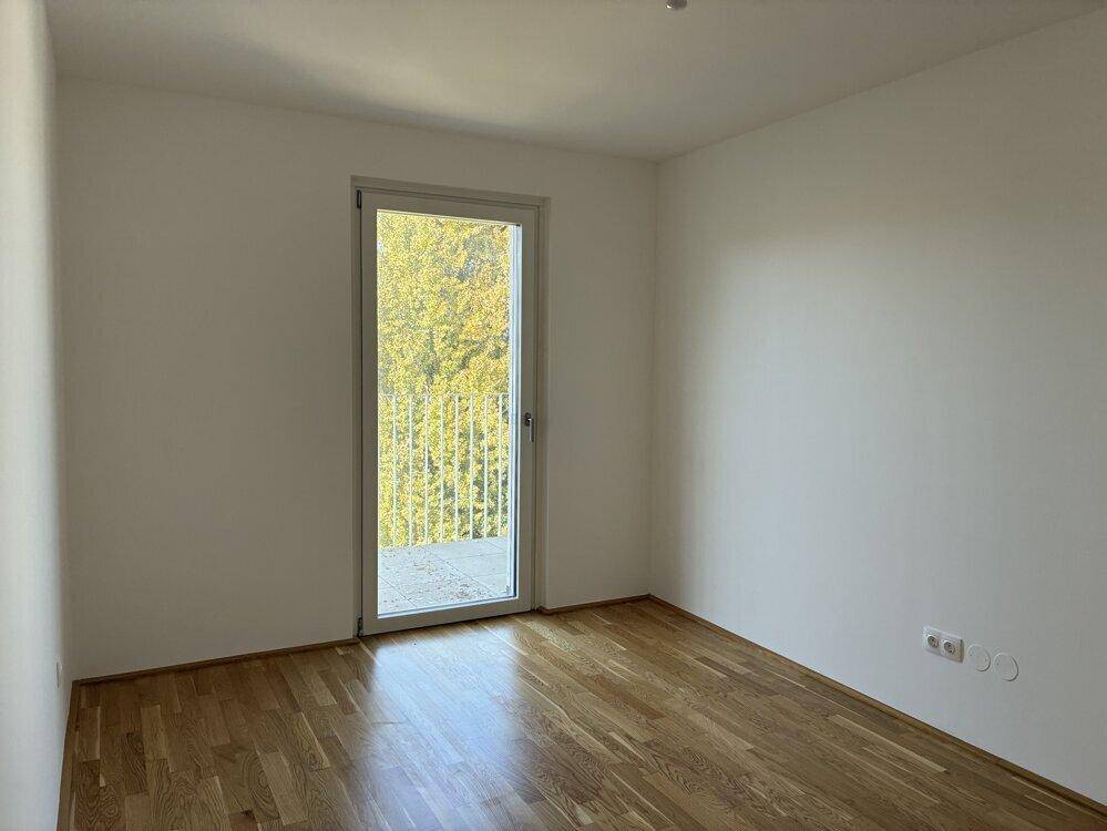 Lichtdurchflutetes Schlafzimmer mit Parkettboden und Zugang zum Balkon, ideal für Entspannung.