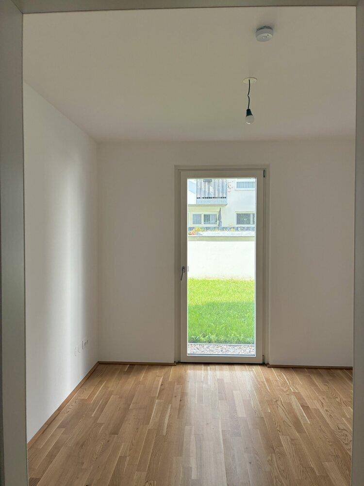 Helles Zimmer mit Holzboden und großer Glastür, die den Blick ins Grüne freigibt und viel Licht spendet.