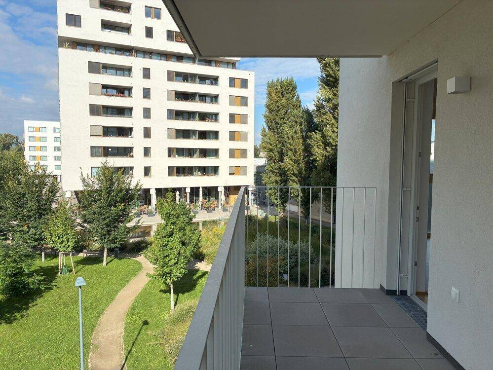 Balkon mit Fliesenboden und Blick auf den grünen Innenhof und umliegende Gebäude.
