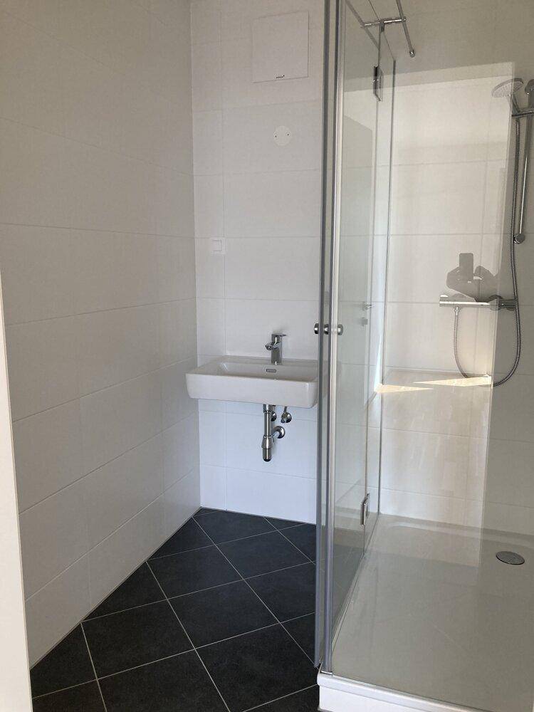 Modernes Badezimmer mit ebenerdiger Dusche, Waschbecken und dunklem Fliesenboden.