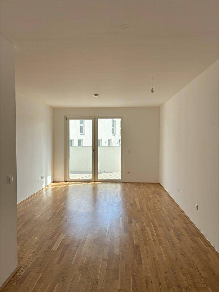 Geräumiges, helles Wohnzimmer mit Holzboden und großen Fenstern, die viel Licht hereinlassen.