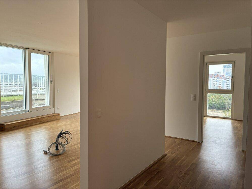 Blick vom Flur in ein helles Wohnzimmer mit großen Fenstern und einen weiteren Raum.